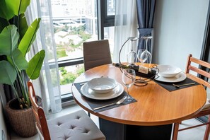 A dining table with white plates, a bottle, and wine glasses, set on a wooden table with a view of buildings outside.