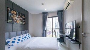 Moderni hotellihuone, jossa on suuri sänky, seinälle asennettu televisio ja näkymä kaupunkiin.