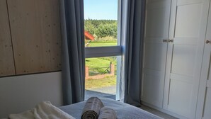A bedroom with a bed, a window with curtains, and a view of a green landscape. - Scandinavian Villa with sauna and hot tube and big garden. (Kołczewo)