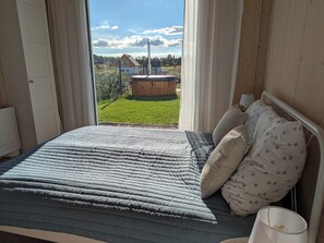 Une chambre à coucher avec un lit, des oreillers, une lampe de chevet et une vue sur un espace verdoyant avec un bâtiment et des arbres.
