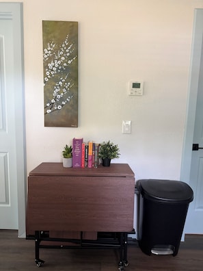 Quarto com armário de madeira, lixeira, termostato e um quadro na parede.