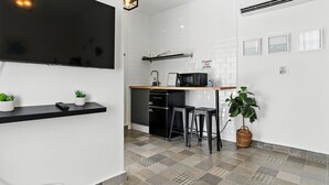 A modern kitchen with a black refrigerator, microwave, and a black countertop. There are two potted plants, a TV mounted on the wall, and a basket with a plant on the floor. - 1BR 1BA Sleeps 2 Wi-Fi La Placita (San Juan)