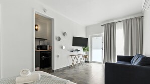 Une chambre d’hôtel moderne équipée d’un lit, d’un canapé, d’une télévision et d’une petite kitchenette, ainsi que d’une porte coulissante donnant sur l’extérieur.