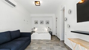 Une chambre à coucher moderne avec un lit, un canapé foncé, une télévision et un revêtement de sol à motifs.
