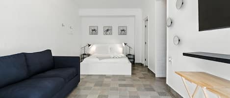 Un dormitorio moderno con cama, sofá oscuro, televisor y suelo estampado.