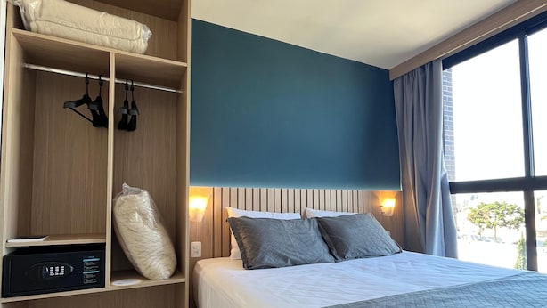 Hotellihuone, jossa on sänky, vaatekaappi, ohjauspaneeli ja ikkuna, jossa on verhot.