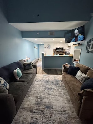 A living room with two sofas, a coffee table, and a TV mounted on the wall. - Oceanfront Escape w/ Balcony + 4 pools (Orange Beach)