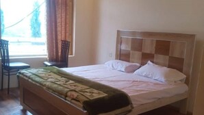 A single bed with a wooden headboard, a bedside table, and a chair. - Hunza Nimbus hotel  (Karimabad)