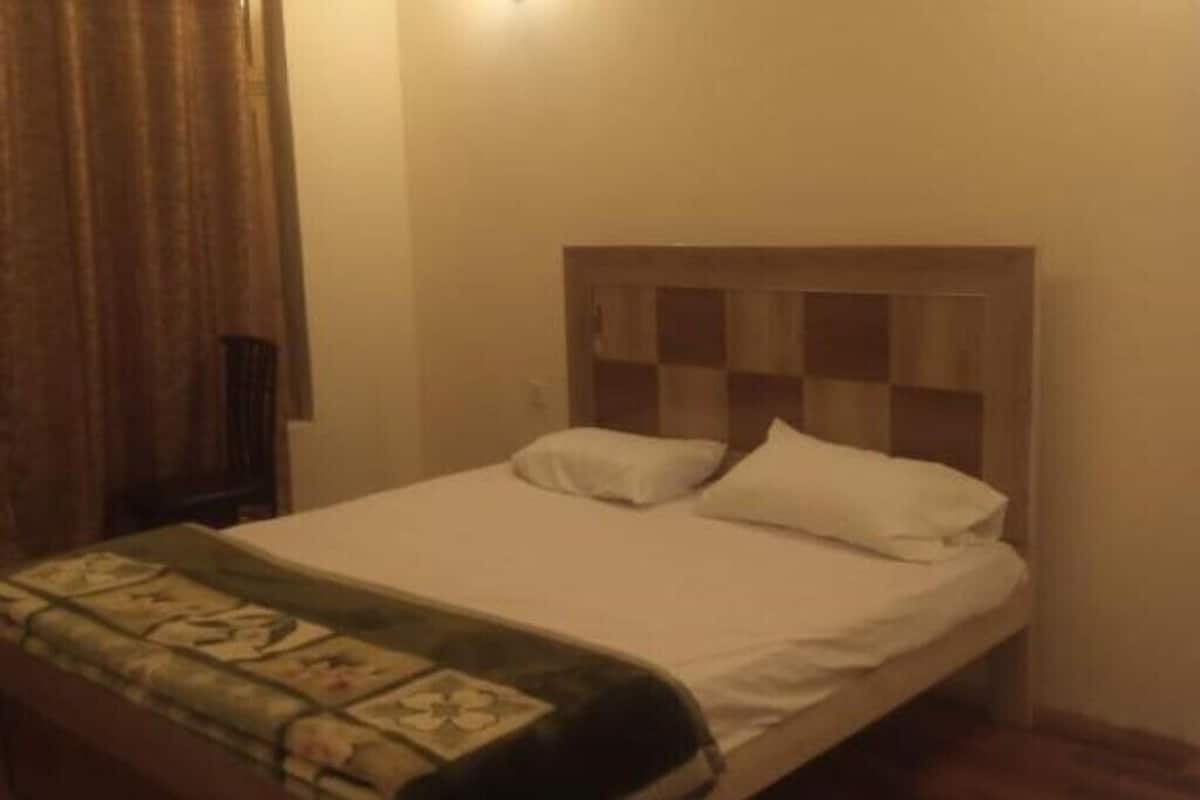 Uma cama de solteiro com cabeceira xadrez, um edredom branco liso e um manta estampada com flores no pé da cama.