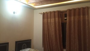A room with a wooden ceiling, a window with brown curtains, and a wall-mounted light fixture. - Hunza Nimbus hotel  (Karimabad)