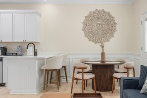 A kitchen with white cabinets, a coffee bar, and a dining area with a round table and four chairs. - Modern 3BR | Heart of Ventnor | Beach Gear Incl (Ventnor City)