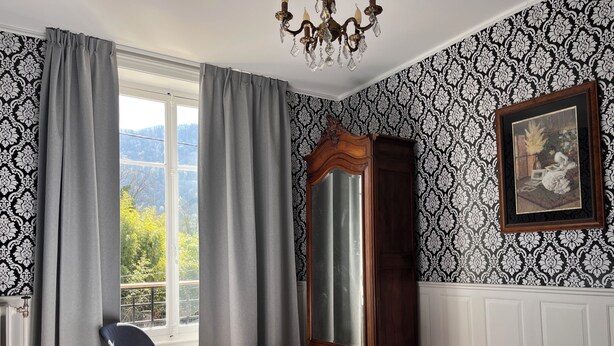 Une chambre à coucher avec un grand lit, une commode, un miroir et une fenêtre avec des rideaux.