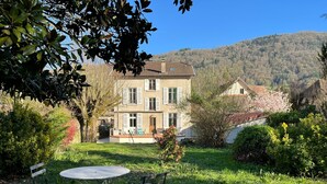 Un bâtiment à deux étages doté d’un patio avec jardin, d’un espace extérieur aménagé pour s’asseoir et offrant une vue sur un paysage vallonné.