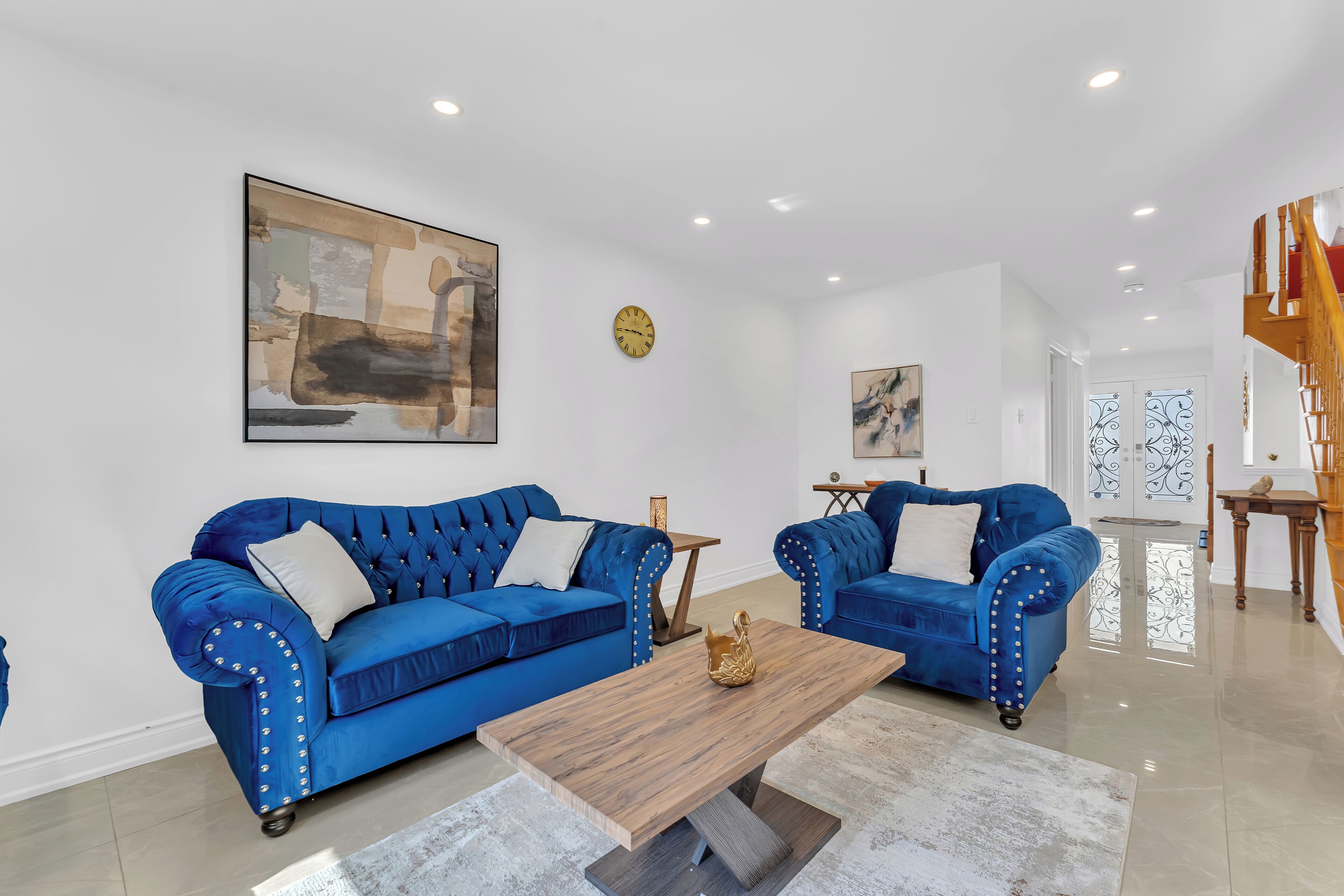 A living room with two blue upholstered sofas, a wooden coffee table, and a large abstract painting on the wall.