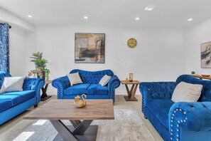 A living room with two blue sofas, a wooden coffee table, and a wall clock. - Norval Cozy Rentals - Luxury - 5 Mins Mount Pleasant (Brampton)