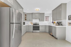 A modern kitchen with grey cabinets, stainless steel appliances, and a tiled floor. - Norval Cozy Rentals - Luxury - 5 Mins Mount Pleasant (Brampton)