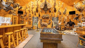 A wooden interior with a bar area, stools, a foosball table, and various mounted animal heads.