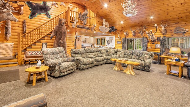 A log cabin interior with a large sectional sofa, a wooden staircase, and various animal taxidermy mounted on the walls.