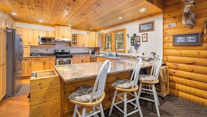 A log cabin kitchen with wooden cabinets, a granite countertop, a mounted deer head, and a refrigerator.