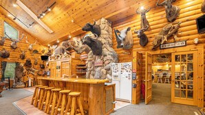 A log cabin interior with a bar area, stools, and various animal heads mounted on the walls.
