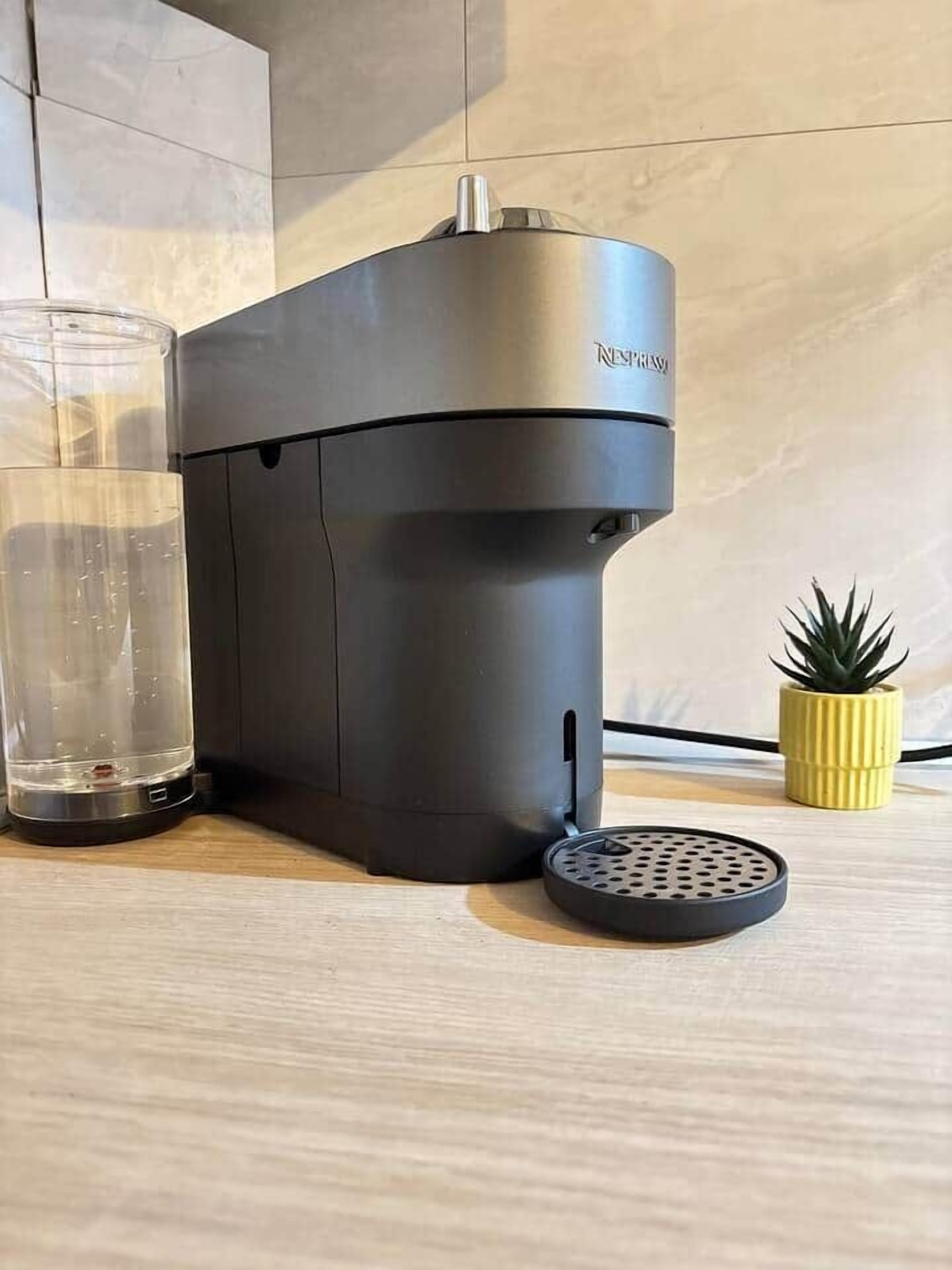 Een koffieapparaat op een aanrecht, met een glas water en een plant in een pot in de buurt.