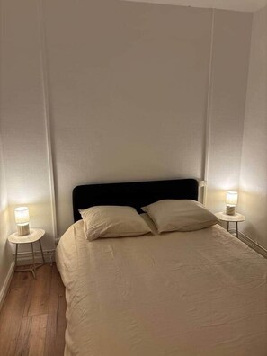 Un lit avec une tête de lit noire, deux lampes de chevet et un plancher en bois.