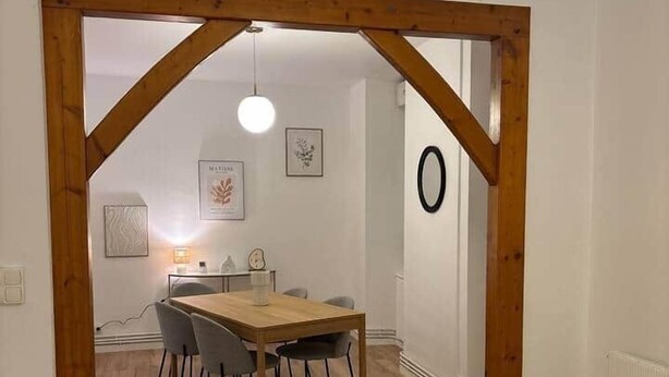 A dining area with a wooden table and chairs, a hanging light fixture, and a white wall with a circular decoration. - Le Parisien - cœur de st-brieuc (Saint-Brieuc)