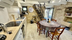 A compact kitchen with a dining area, a clock on the wall, and a staircase leading to an upper level. - The Pechplazen grangette (Rudelle)