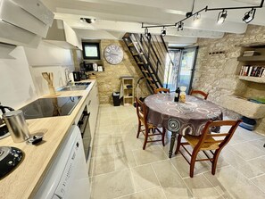 A compact kitchen with a dining area, a clock on the wall, and a staircase leading to an upper level.