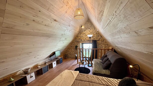A cozy attic bedroom with a sloped ceiling, a stone wall, a wooden floor, a bed, a TV, and a small table. - The Pechplazen grangette (Rudelle)