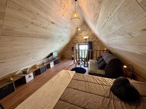 Une chambre confortable située dans les combles, avec un plafond en pente, un mur en pierre, un plancher en bois, un lit, une télévision et une petite table.