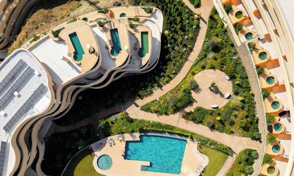Eine Vogelperspektive zeigt ein Resort mit mehreren Schwimmbecken, angelegten Gärten und einem großen zentralen Pool.