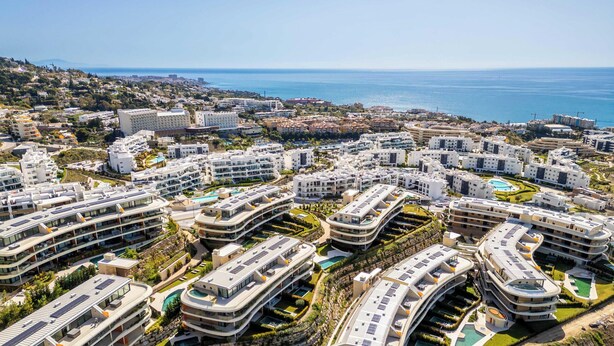 Una zona residencial costera con edificios de apartamentos modernos, algunos con piscinas en la azotea, y una vista despejada del mar.