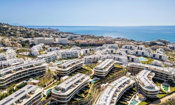 Ein Küstenwohngebiet mit modernen Mehrfamilienhäusern, einige davon mit Dachpools, und freiem Blick auf das Meer.