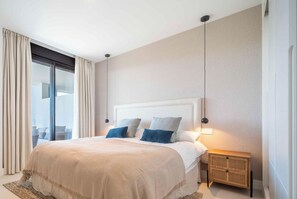 A bedroom with a large bed, a nightstand, a lamp, and a view through a sliding door. - Infinity View by HWPC (Fuengirola)