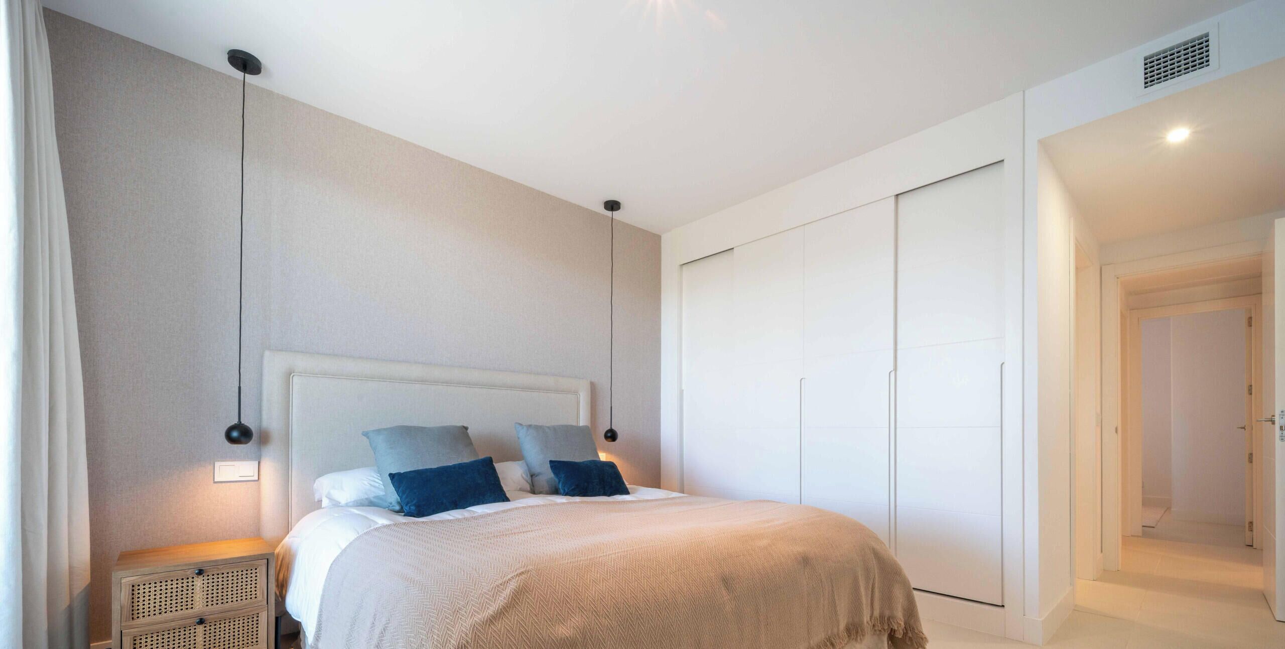 Un dormitorio con cama, mesitas de noche, un armario y una puerta que da a otra habitación.
