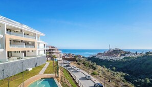 Ein modernes Hotel mit Pool, Meerblick und hügeliger Landschaft im Hintergrund.