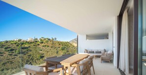 A balcony with a wooden table and chairs, a sofa, and a view of a hillside. - Infinity View by HWPC (Fuengirola)