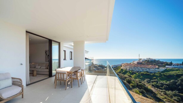 Een balkon met een tafel en stoelen, een bank en uitzicht op zee en gebouwen.