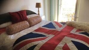 A bed with a Union Jack quilt, a red pillow, and a lamp beside a window. - LOVELY LITTLE NEST FOR UP TO 5 PEOPLE, PETS WELCOME (Nice)