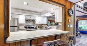 A kitchen with a central island, stainless steel appliances, and wooden paneling. - Pine Loch, cozy cabin sleeps 9 with 3 bedrooms, 2 baths. Gas fire pit on deck. (Pocono Lake)