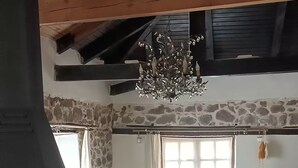 A rustic interior with a stone wall, wooden beams, a chandelier, a fireplace, a sofa, a table, and a chair.