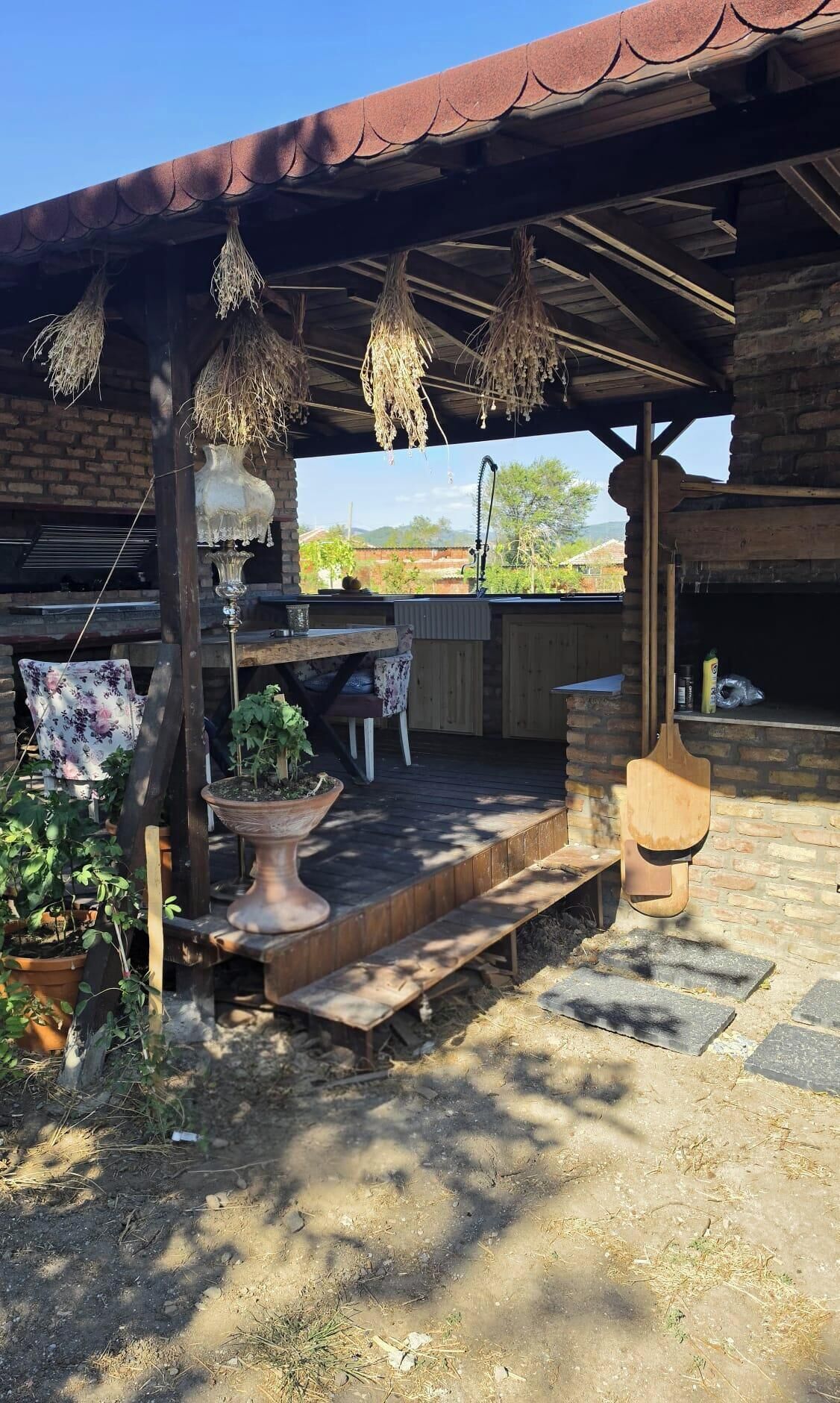 An outdoor patio with a wooden table, chairs, hanging plants, and a brick wall.