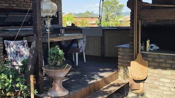 An outdoor patio with a wooden table, chairs, hanging plants, and a brick wall.