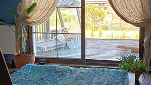 A room with a large window, a bed with a patterned bedspread, and two potted plants.
