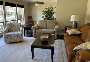 A living room with a sofa, armchair, coffee table, and a potted plant.