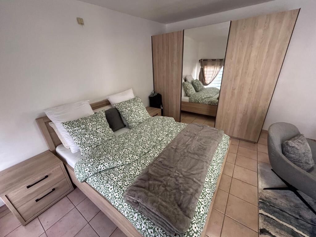 Een slaapkamer met een bed, nachtkastje, stoel en spiegel.