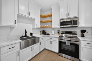 A modern kitchen with white cabinets, stainless steel appliances, and a wooden floor. - Modern Brownsville Duplex Near SPI & Downtown (Brownsville)