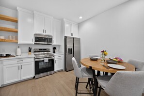 Una cocina moderna con armarios blancos, electrodomésticos de acero inoxidable y una zona de comedor con una mesa redonda y sillas grises.