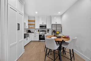 A modern kitchen with white cabinetry, stainless steel appliances, and a round dining table with four chairs.